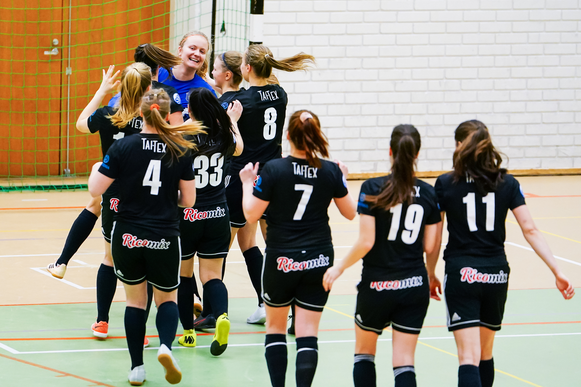 Ett dam inomhusfotbollslag firar ett mål på en inomhusbana.