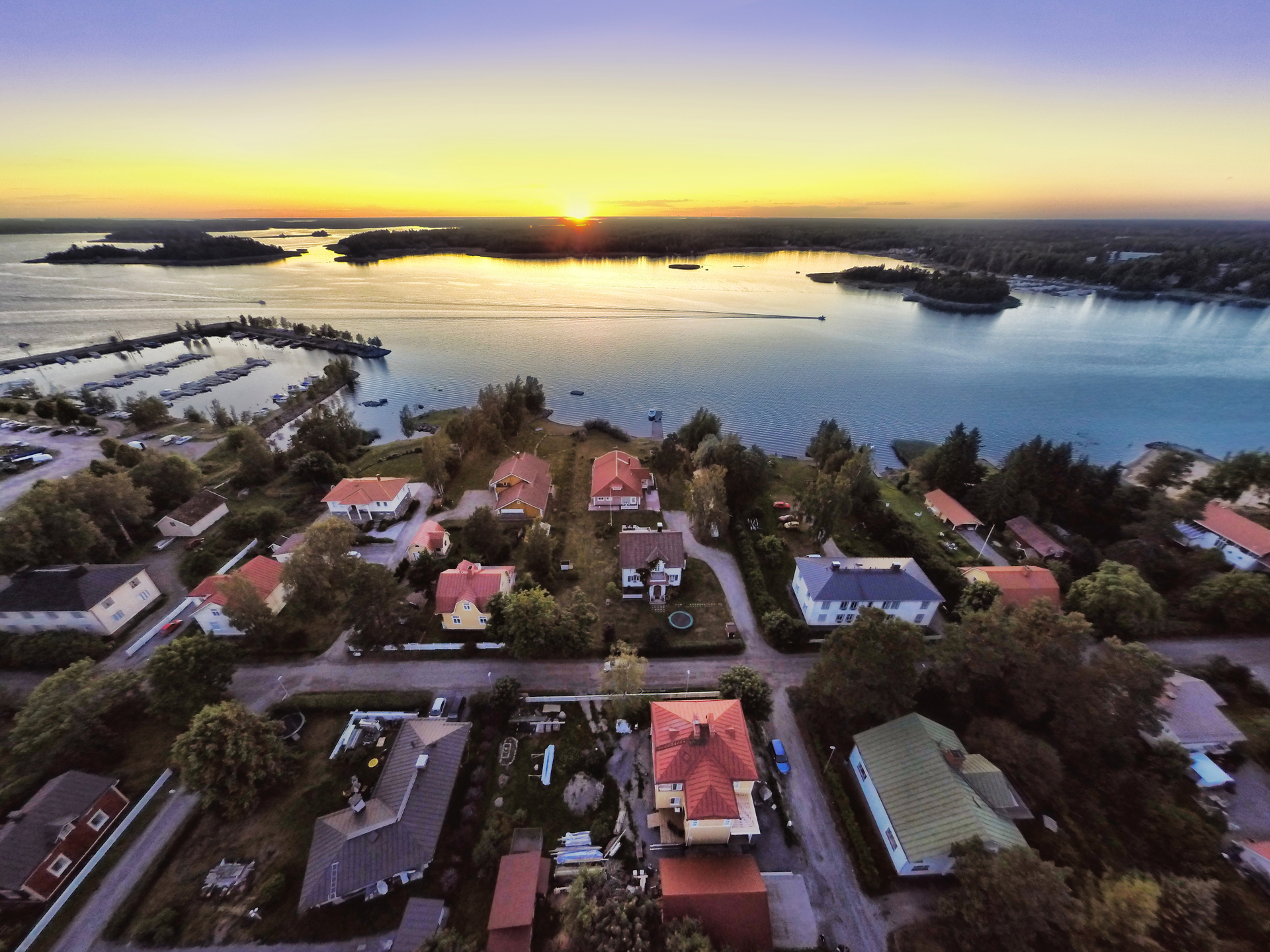 Ilmakuva auringonlaskusta merenrannassa, jossa on asuinalue.