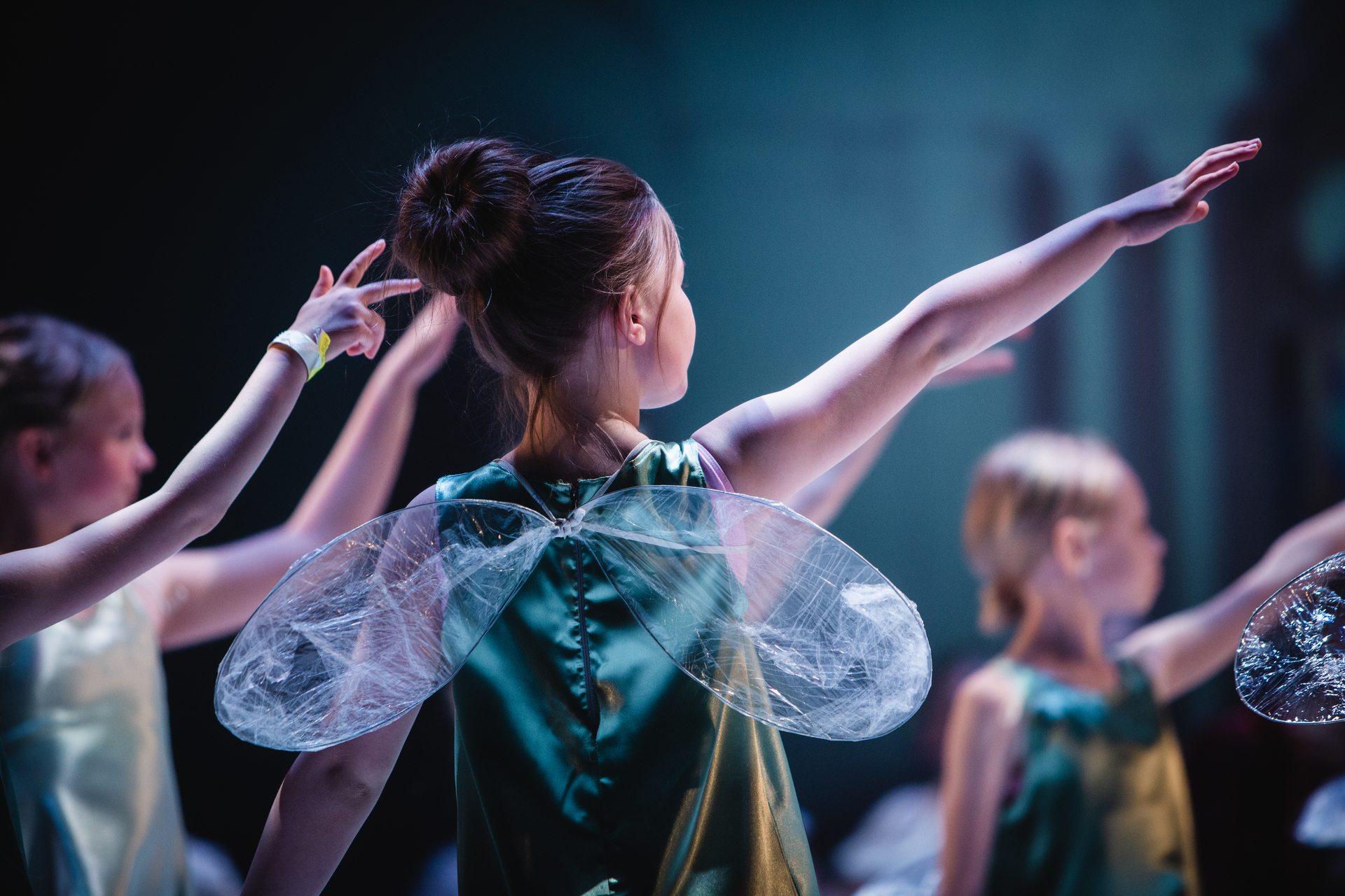 Children performing on stage dressed as fairies with wings and green costumes.