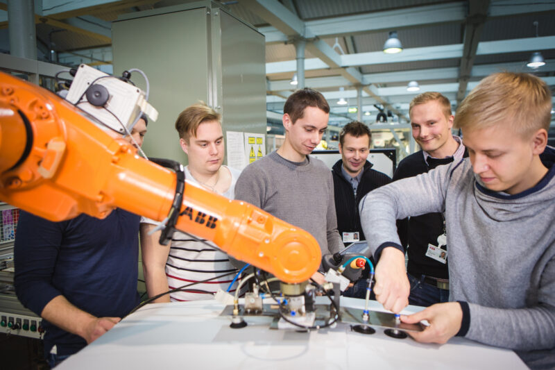 Ryhmä opiskelijoita katsoo vierestä, kun yksi heistä työskentelee robotin parissa.