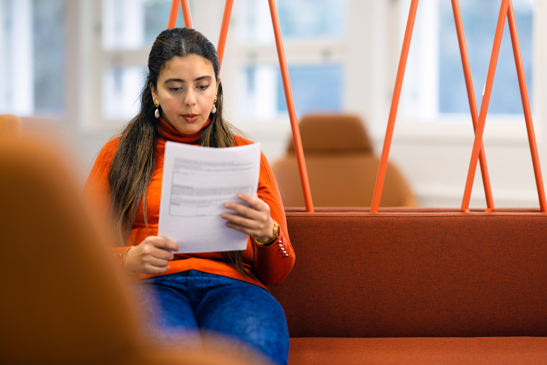 A woman sits on an orange sofa reading a document.