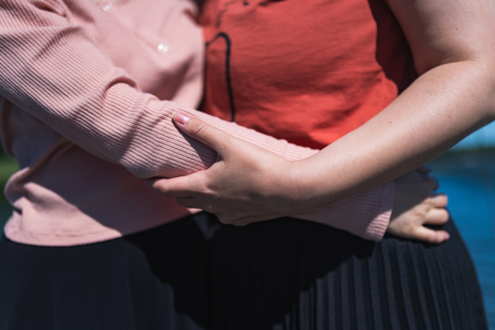 Två personer som kramar varandra utomhus, klädda i rosa och röd topp.
