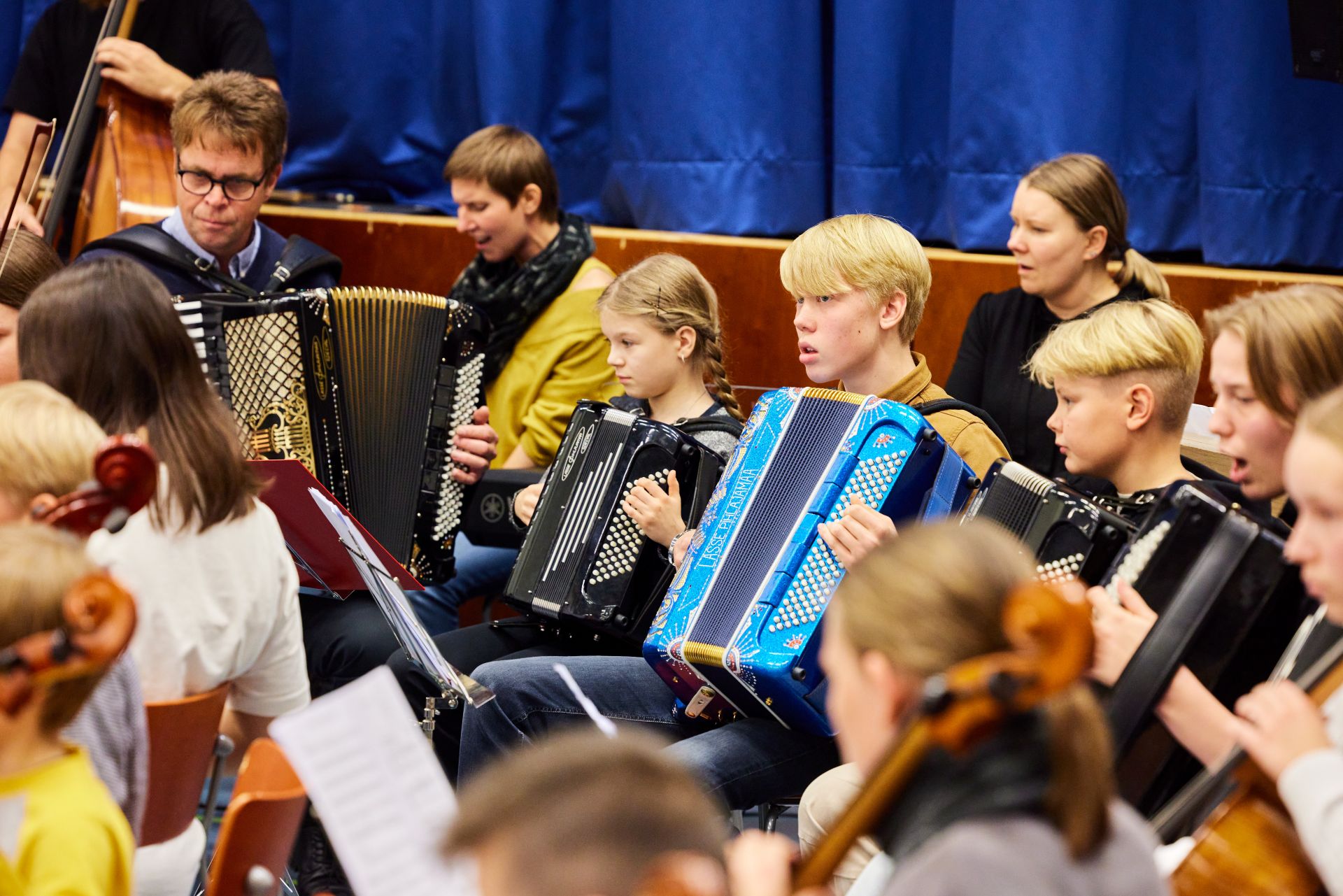 A group of musicians playing accordions and string instruments in a blue performance room.