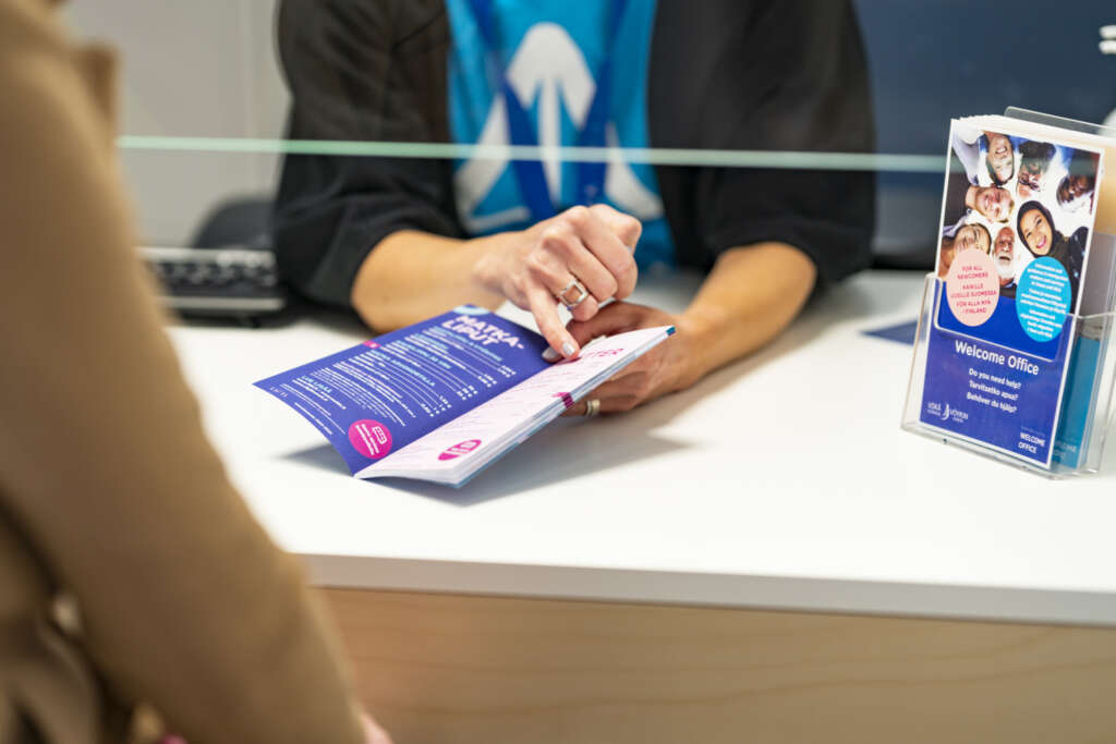 A person guiding a customer with a brochure at a help desk.