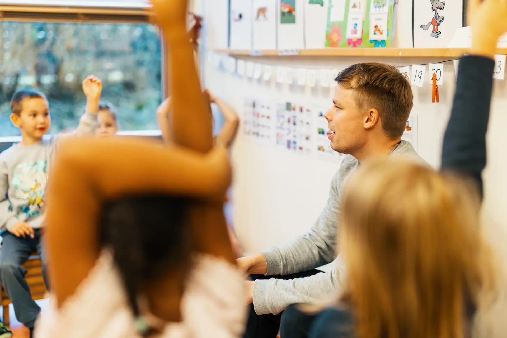 Varhaiskasvatuksen opettaja ja lapset ovat oppitunnilla luokkahuoneessa. Aikuinen istuu la