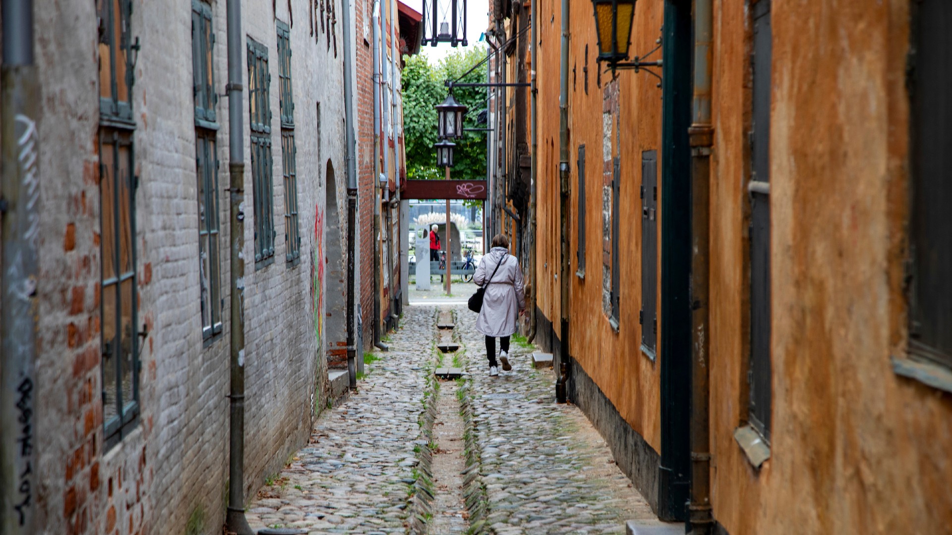 A narrow cobblestone street lined with old brick buildings. A person is walking away from the camera.