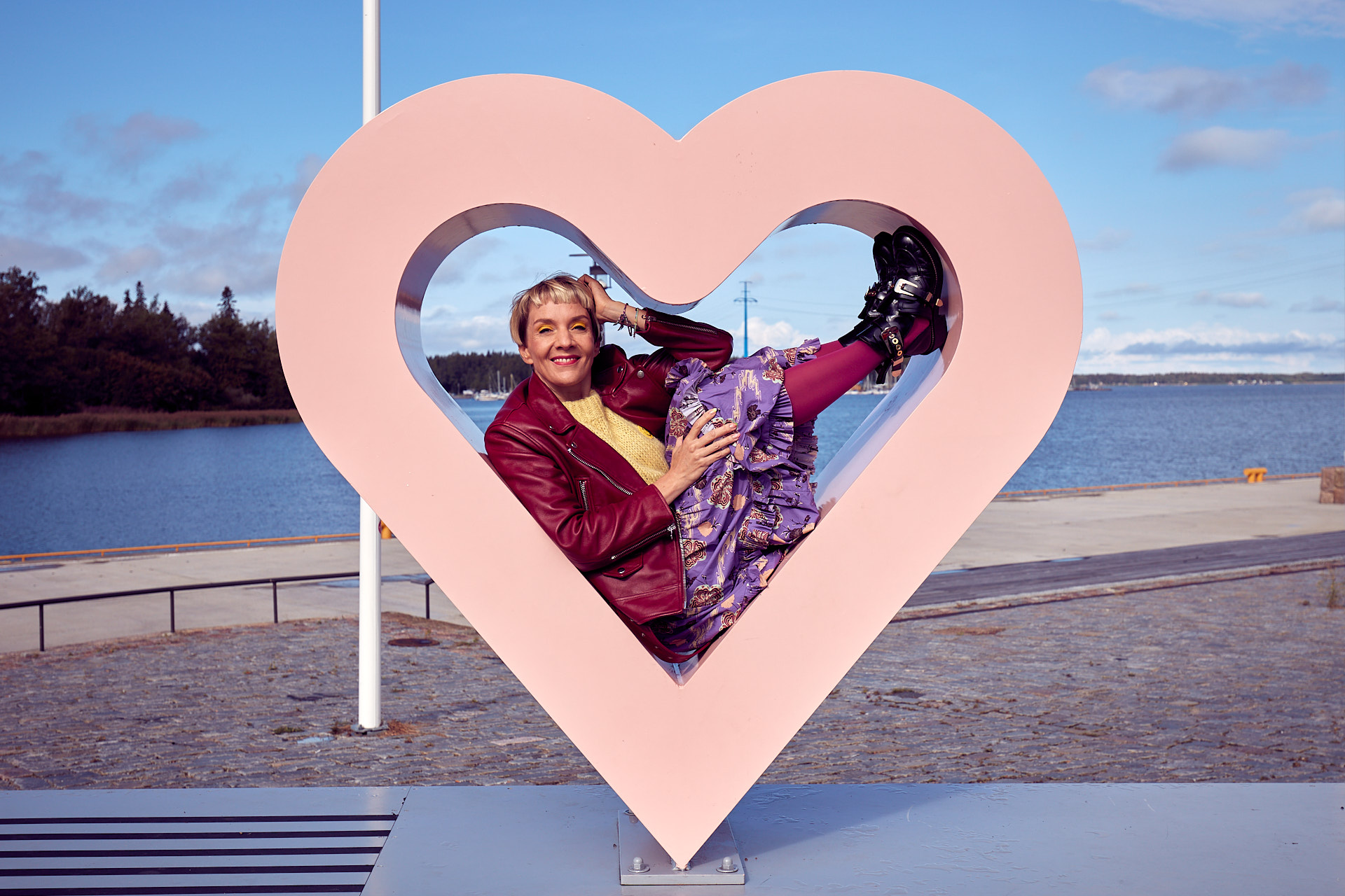 Henkilö poseeraa vaaleanpunaisen sydänveistoksen sisällä merenrannassa.
