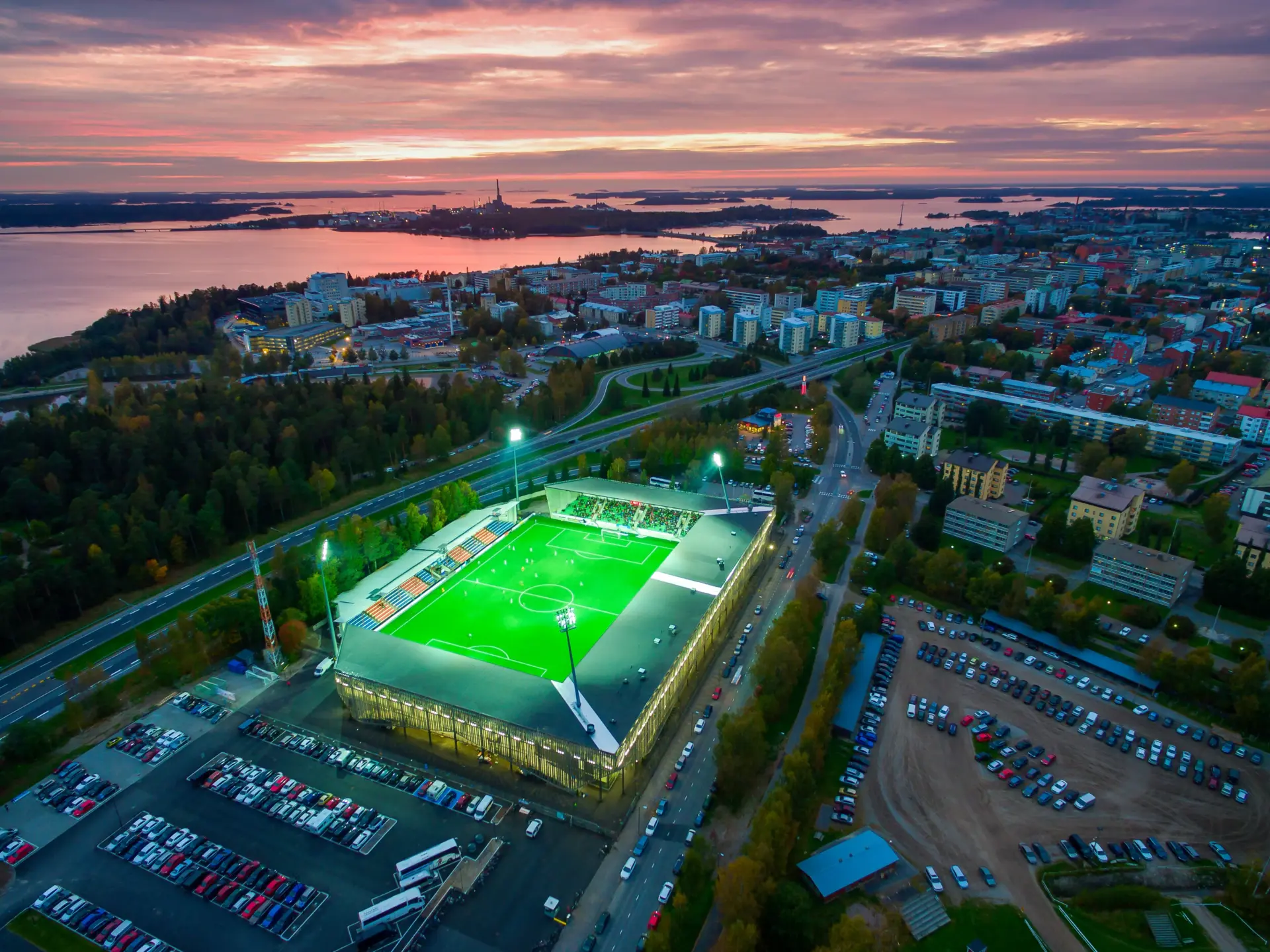 Aerial view of a sports stadium in a city with a sunset in the background.