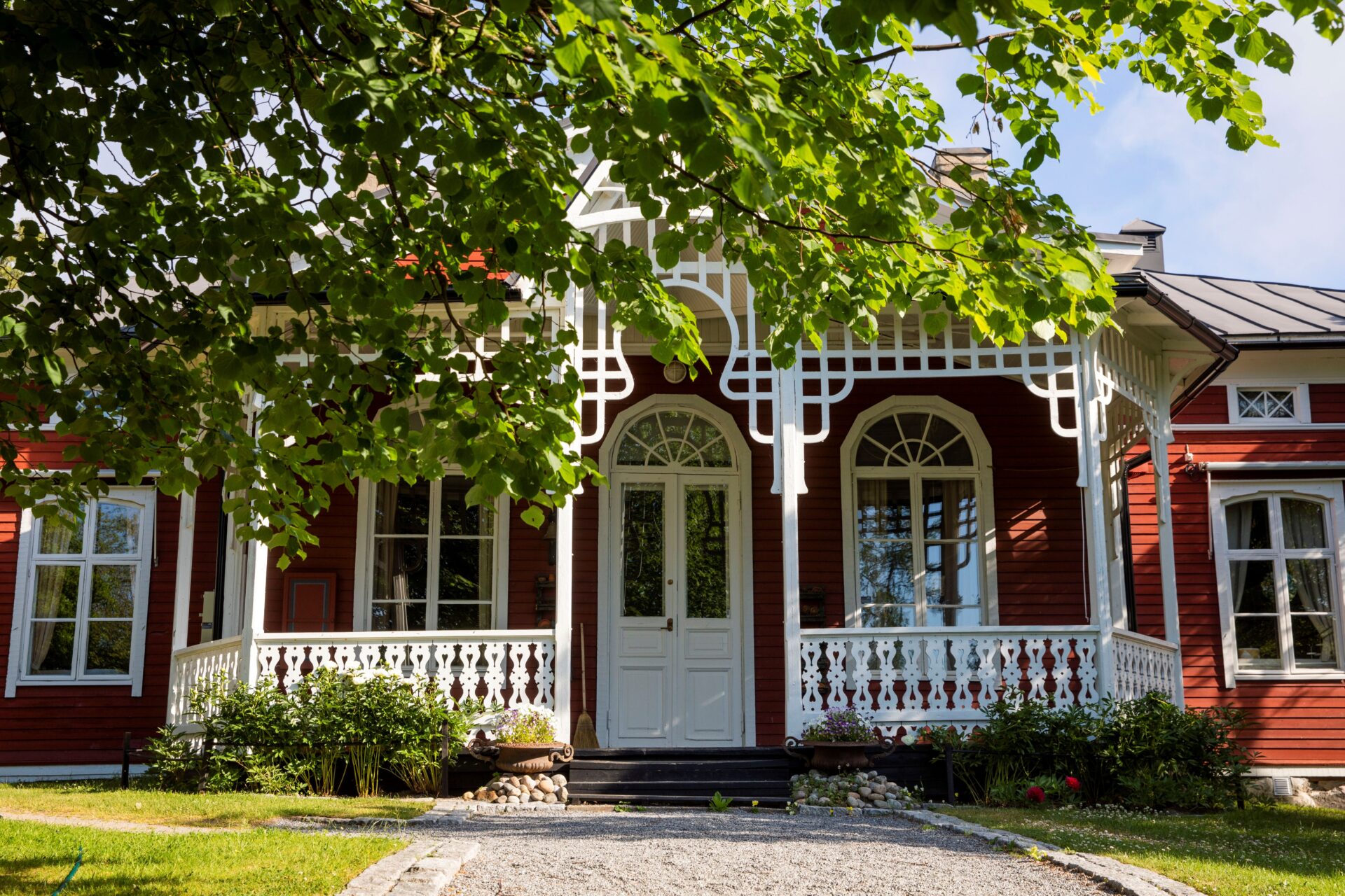 A beautiful red wooden house with a decorative white porch and a lush green yard.
