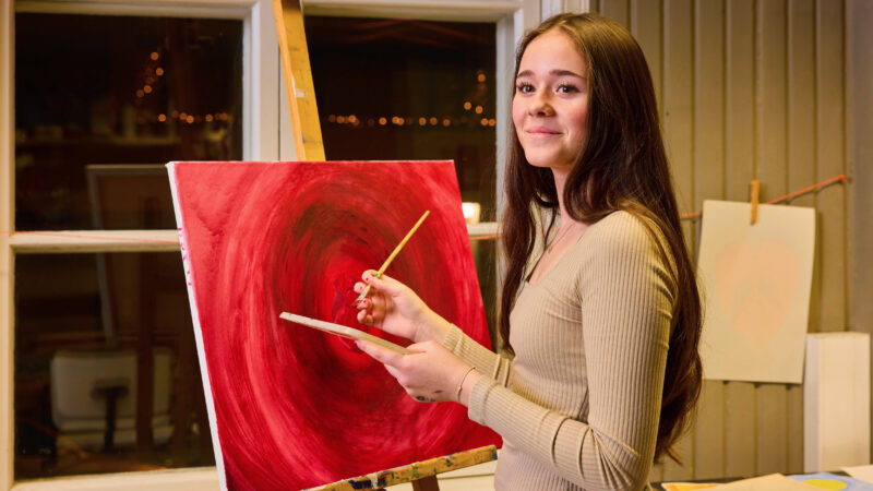 A woman painting an abstract red artwork on an easel.