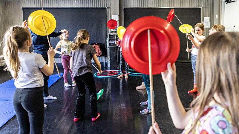 Children practicing spinning plates on sticks in a gym space.