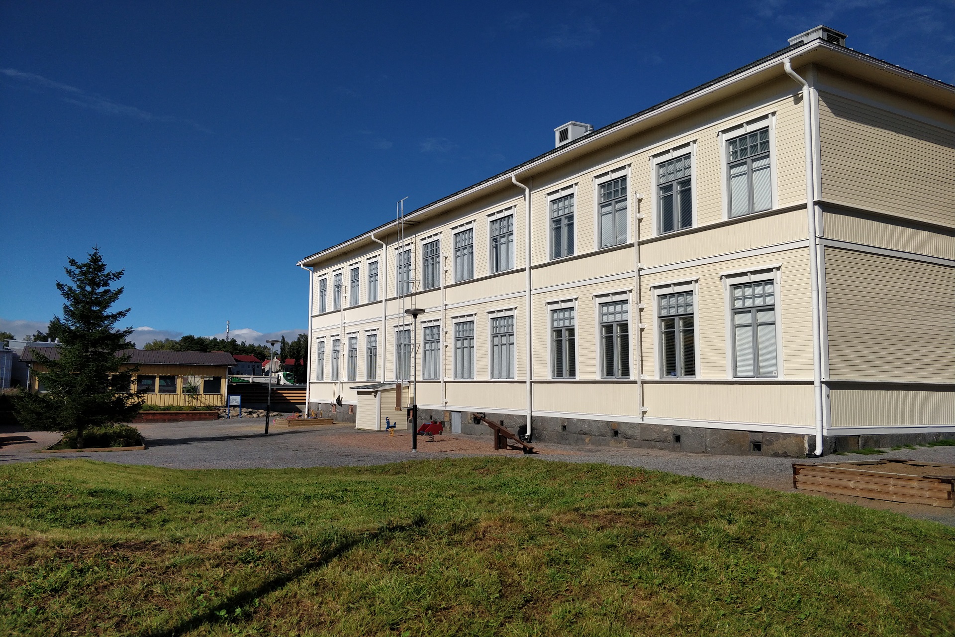 Ljust tvåvånings trähus i solsken med blå himmel.