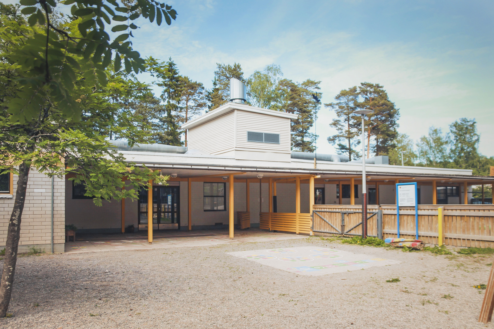 Byggnad omgivet av träd med ljus fasad och täckt veranda.