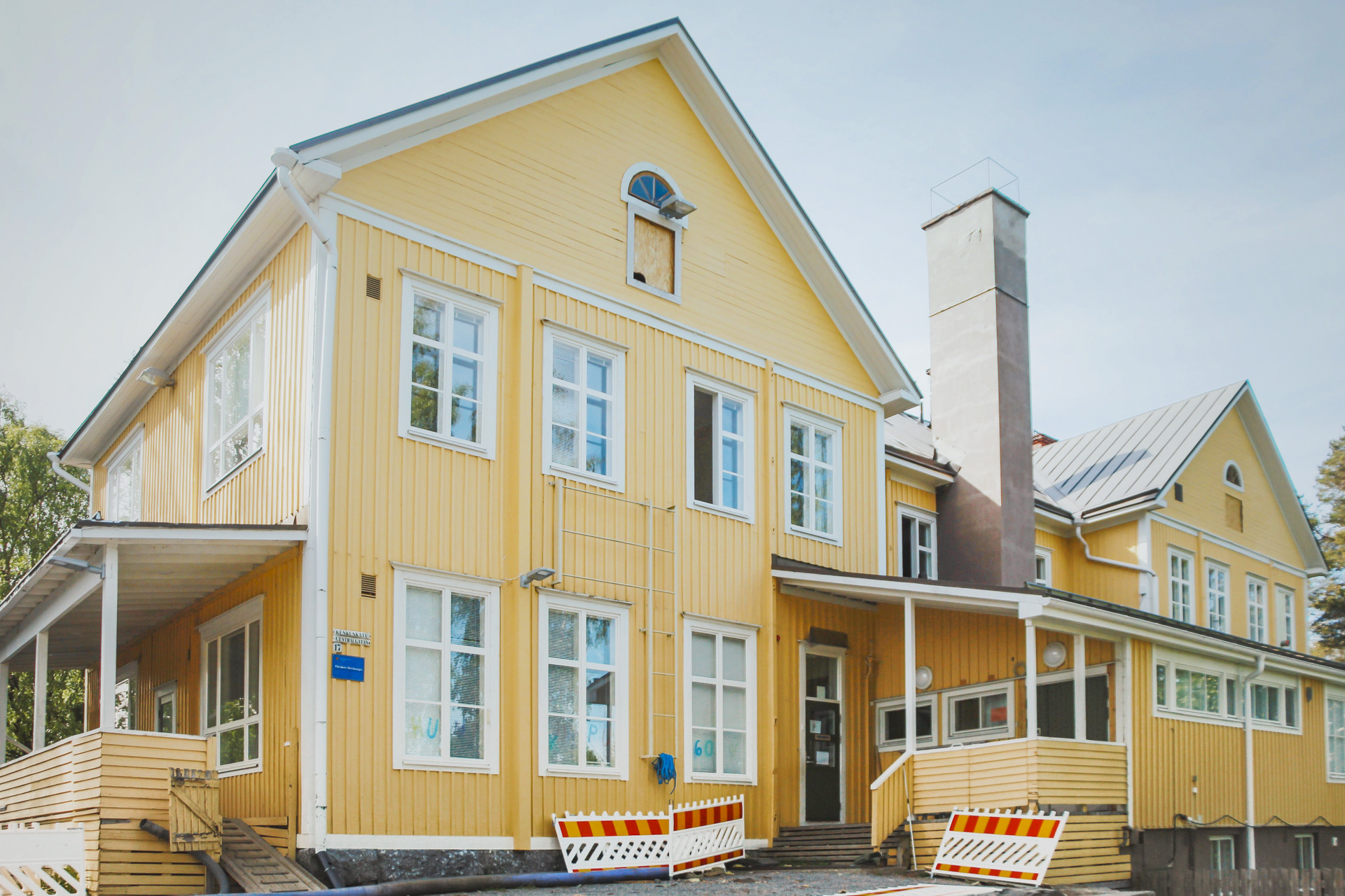 Gult trähus med vita fönsterkarmar och grått tak. Framför huset finns orange‑vita hinder.