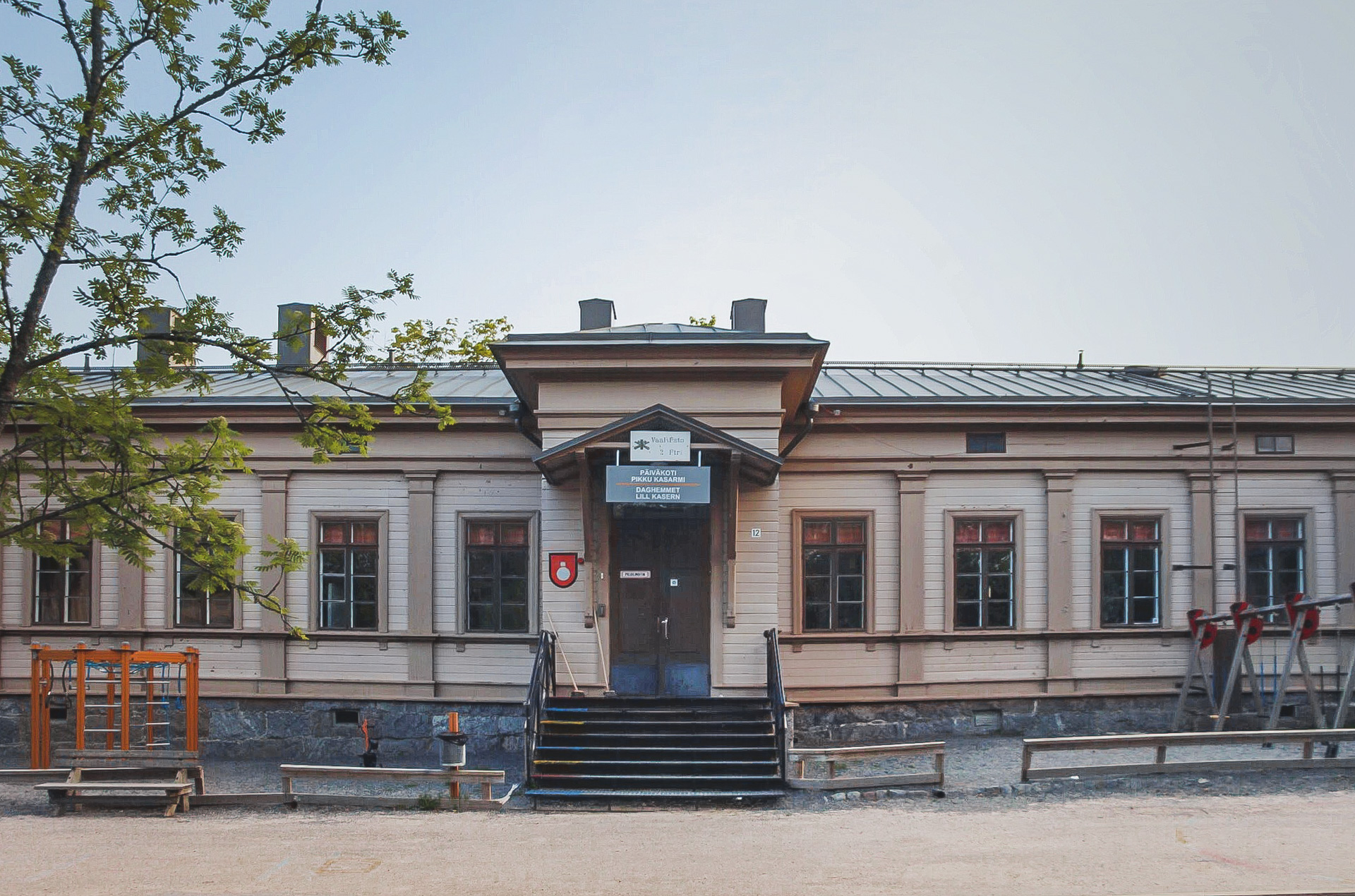 Gammal träbyggnad med flera fönster och liten trappa. Skylt med 'Päiväkoti' framme.