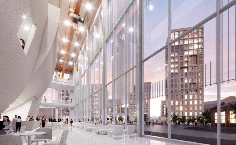 A modern building interior with tall windows and bright spaces. A tall building is visible outside against a sunset sky.