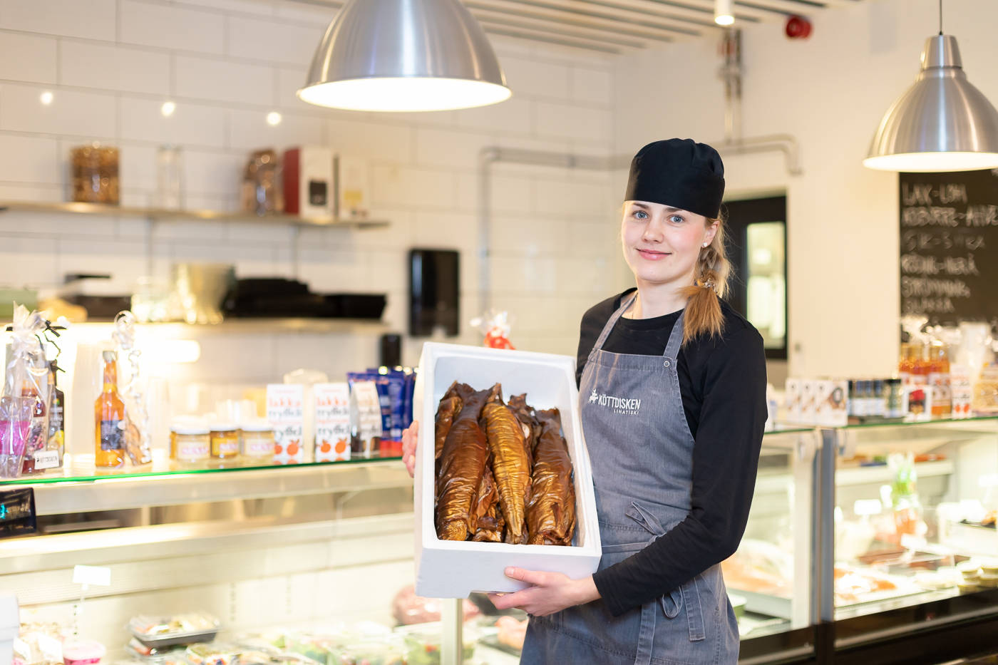 En kvinna som håller en låda med rökt fisk i en butik.