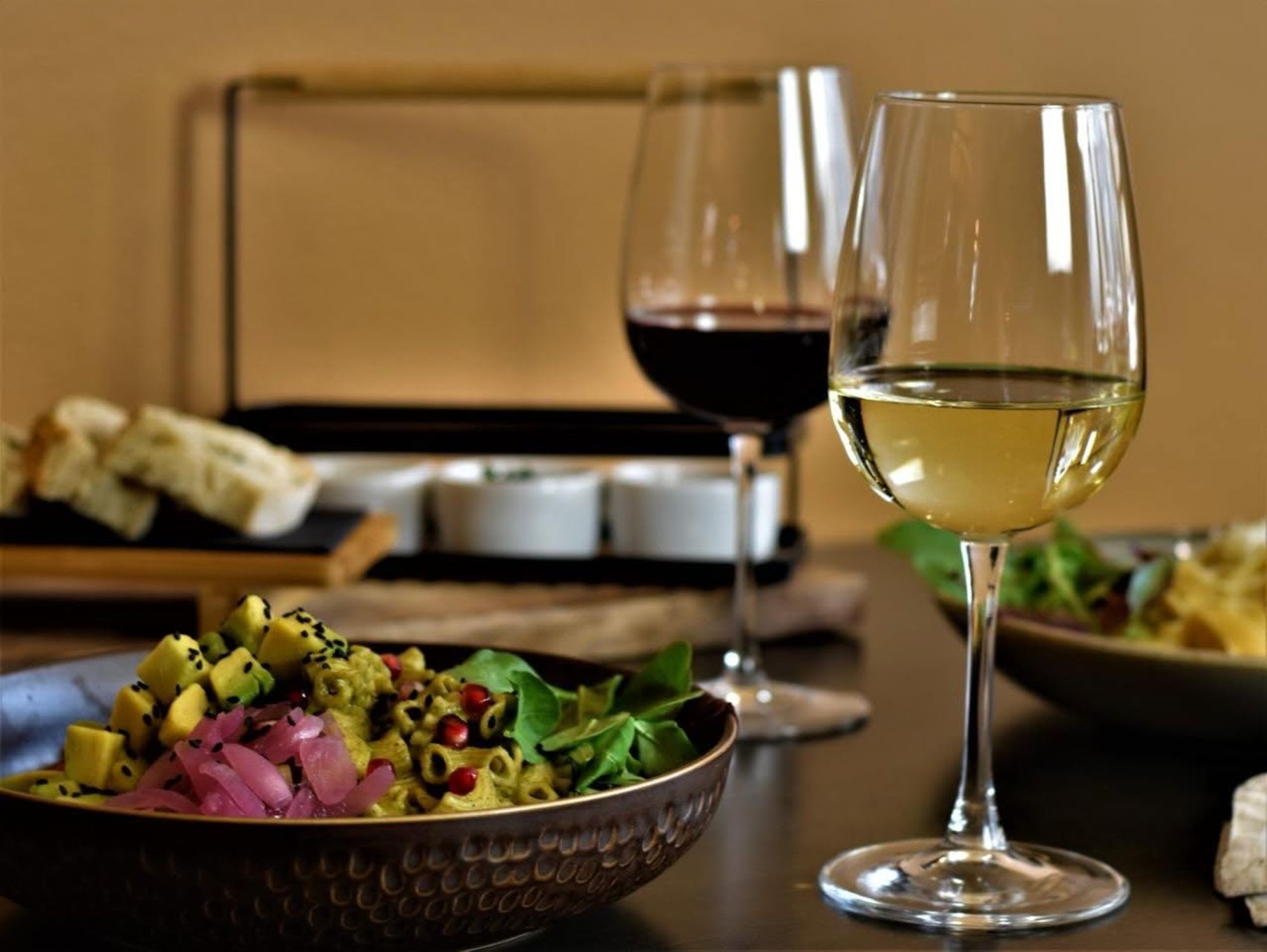 Två vinglas, ett med vitt vin och ett med rött vin, står på ett bord med en tallrik sallad och brödskivor i bakgrunden.