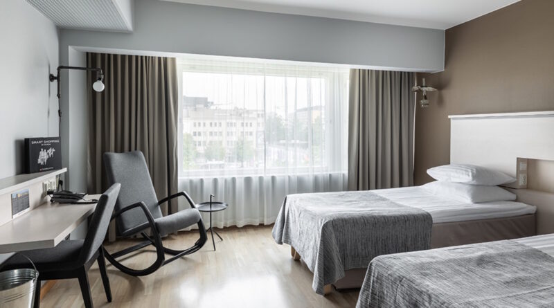 Hotellihuone, jossa on kaksi sänkyä ja suuri ikkuna. Huone on sisustettu vaaleilla sävyillä ja siinä on moderni sisustus.
