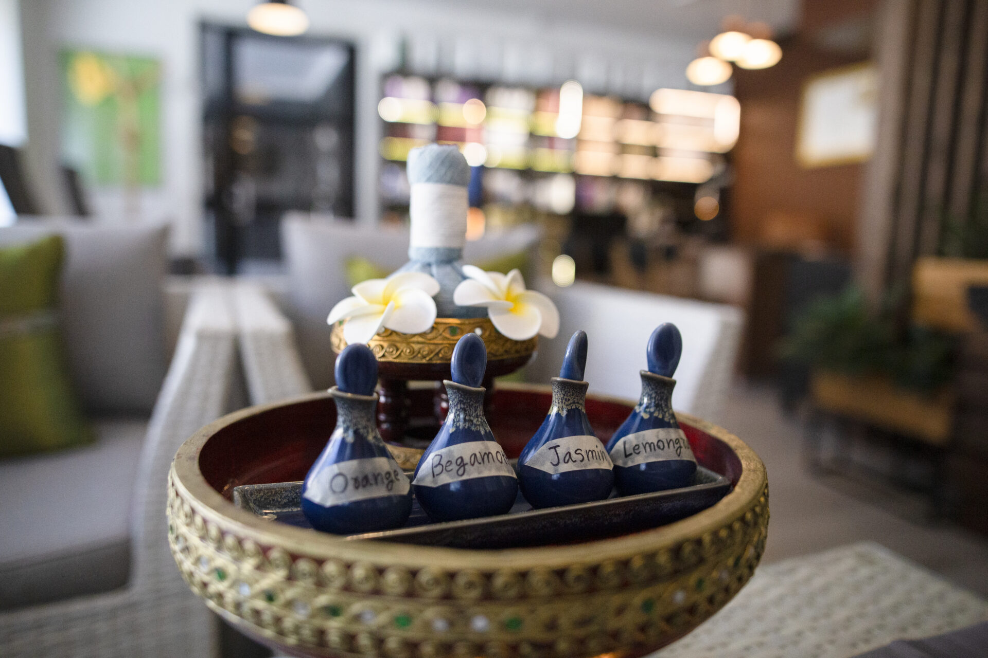 Decorative tray with blue bottles labeled 'Orange', 'Bergamot', 'Jasmine' and 'Lemongrass', and white flowers in a cozy room.