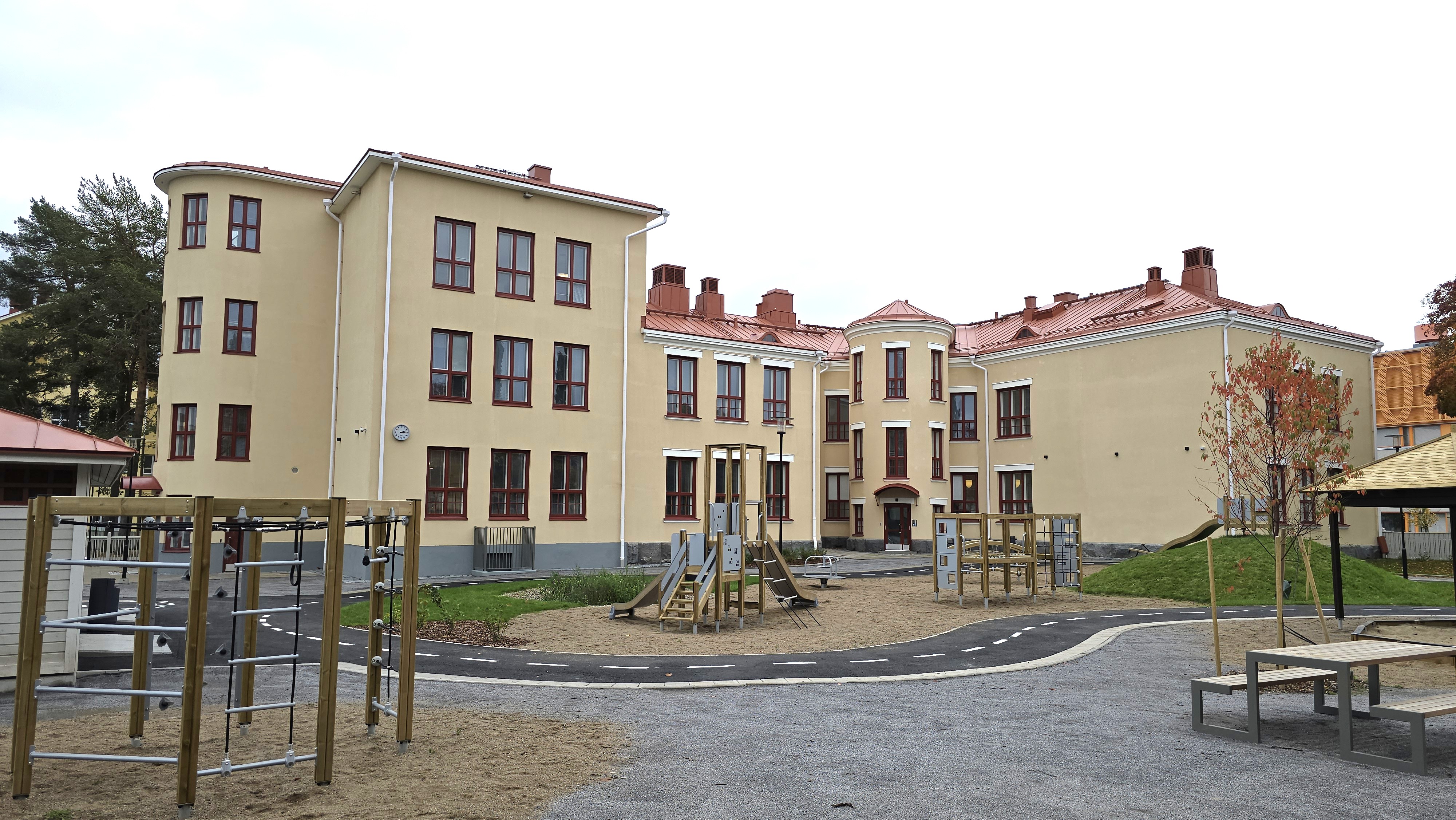 En daghemsgård med en lekplats och en stor, ljusgul daghemsbyggnad.