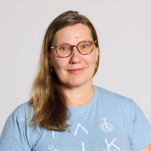 Woman with glasses and long hair, wearing a light blue t-shirt.