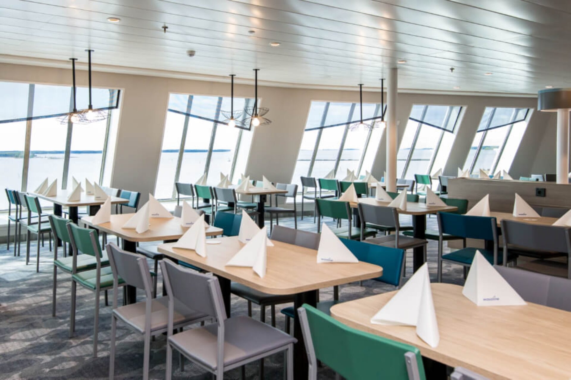 Restaurangsal med flera bord och stolar, utsikt mot havet genom stora fönster.