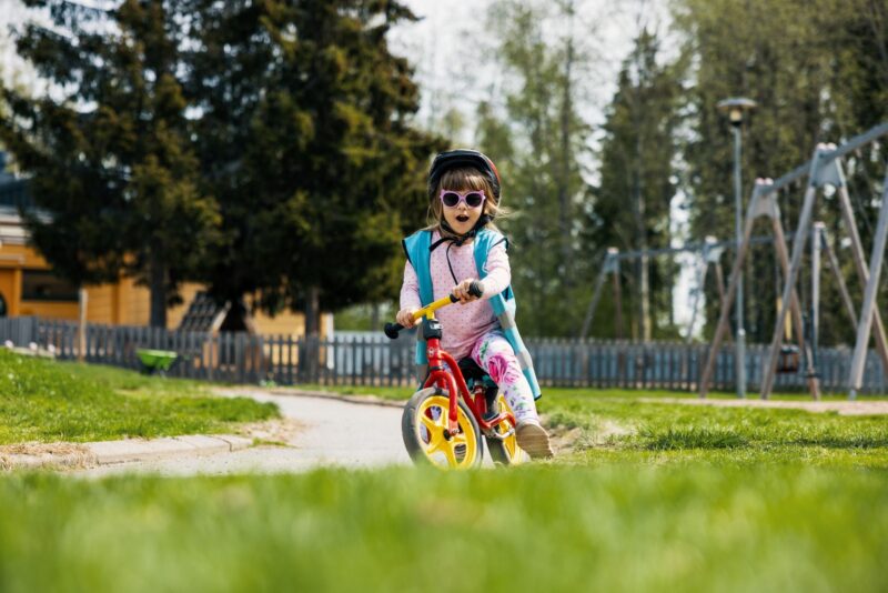 Ett barn cyklar på en lekplats en solig dag.