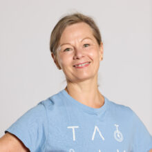 A woman smiling and standing wearing a light blue t-shirt.