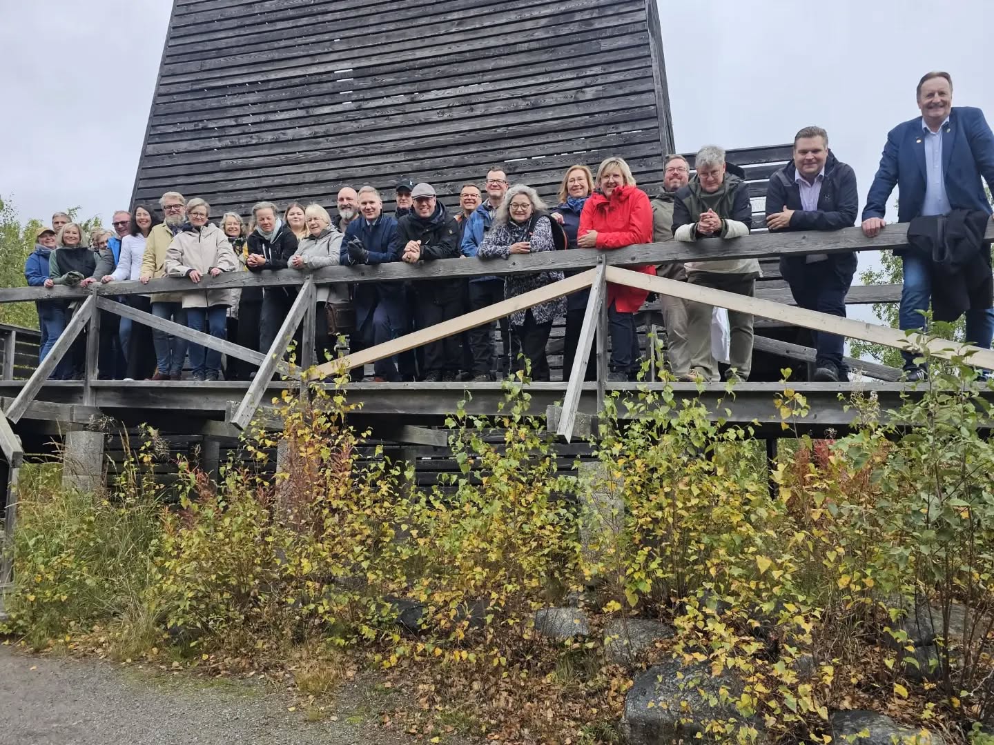A group of people standing on a wooden balcony in front of a large wooden building.