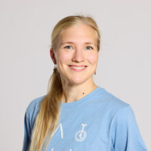 A person with blonde hair smiling in a light blue shirt.